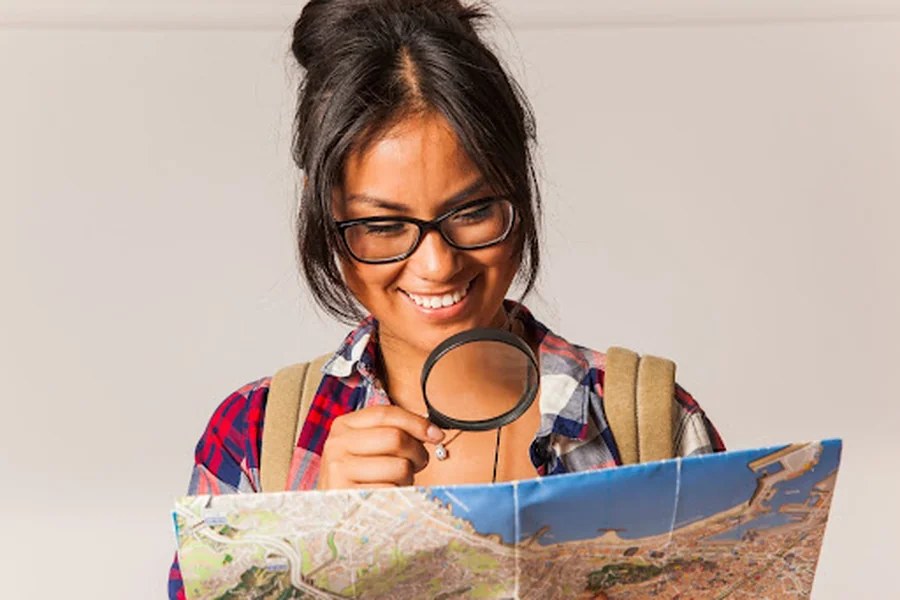 Woman using a magnifying glass to inspect a city map, representing how proximity, prominence, and relevance influence local search visibility.